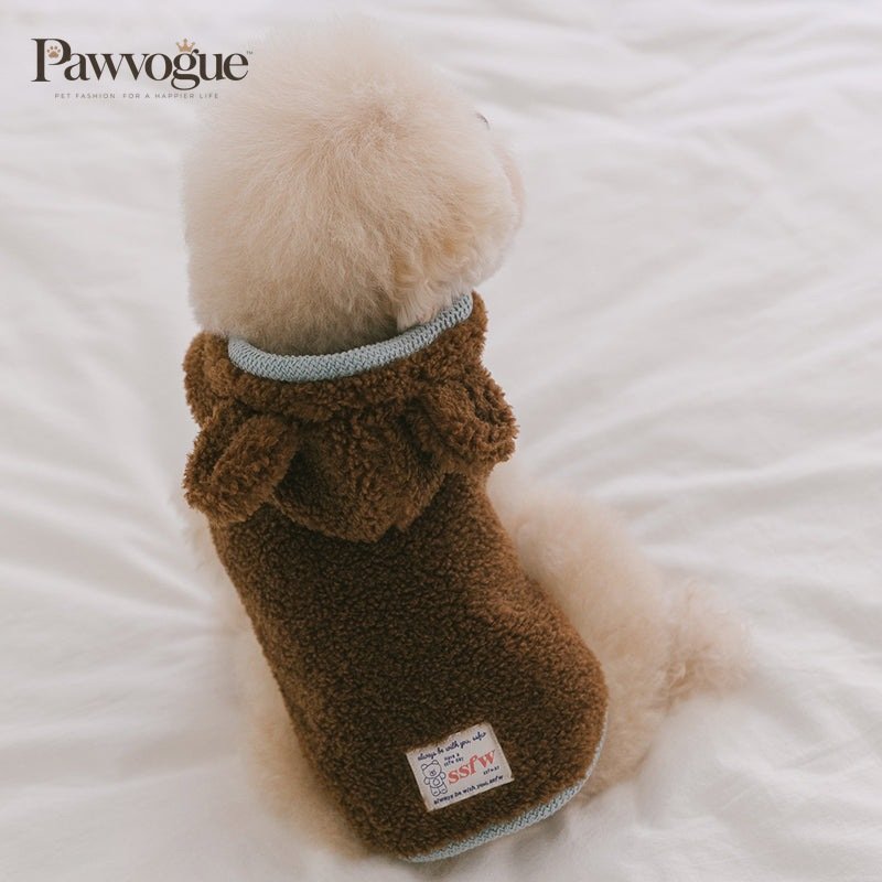 Dog wearing a brown fleece sweater with a brand label on a white surface